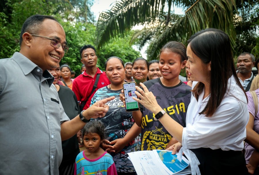 Deputy Communications Minister Teo Nie Ching (right) looking at a smart phone belonging to a resident of Kampung Orang Asli Kerling after the completion of the “Proof of Concept” Starlink communications tower. Bernama picture