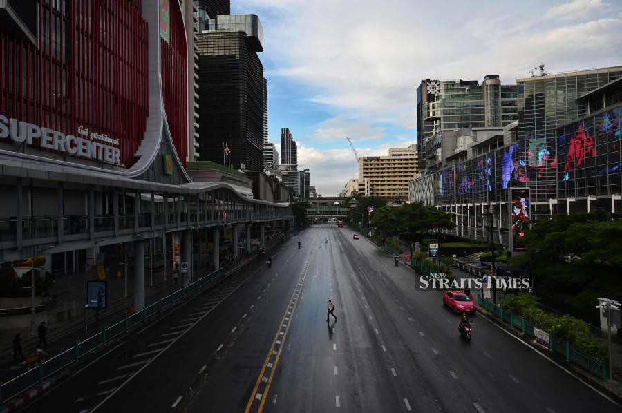 A man crosses the road on Ratchaprasong intersection in Bangkok on July 12, 2021, on the first day of stricter lockdown restrictions to try to contain the spread of the Covid-19 coronavirus. Thailand has approved the use of green chiretta to treat asymptomatic Covid-19 patients after a successful trial conducted by the Corrections Department with infected prisoners. (Photo by Lillian SUWANRUMPHA / AFP)