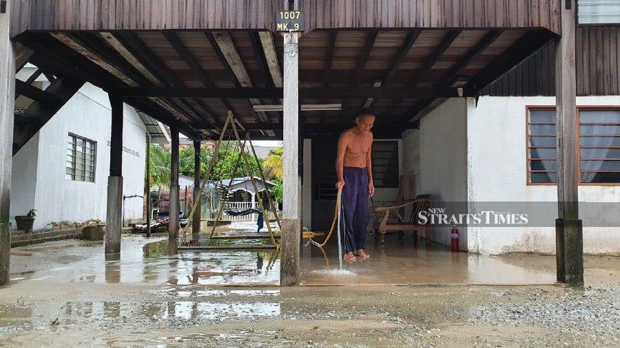 A resident in Kampung Sulup, Teluk Kumbar, seen cleaning his porch following the flood. - NSTP/MIKAIL ONG