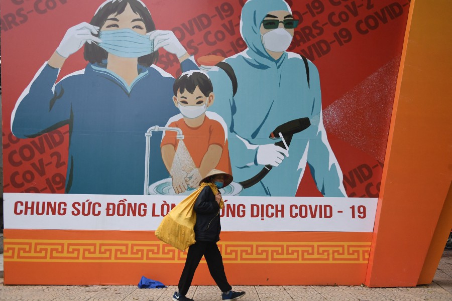 A woman walks past a billboard with information on preventing the spread of the Covid-19 coronavirus in Hanoi. - AFP PIC