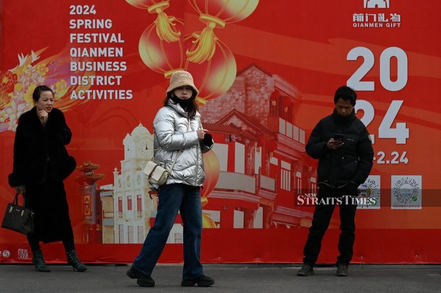 People walk along a shopping street in Beijing. - AFP PIC