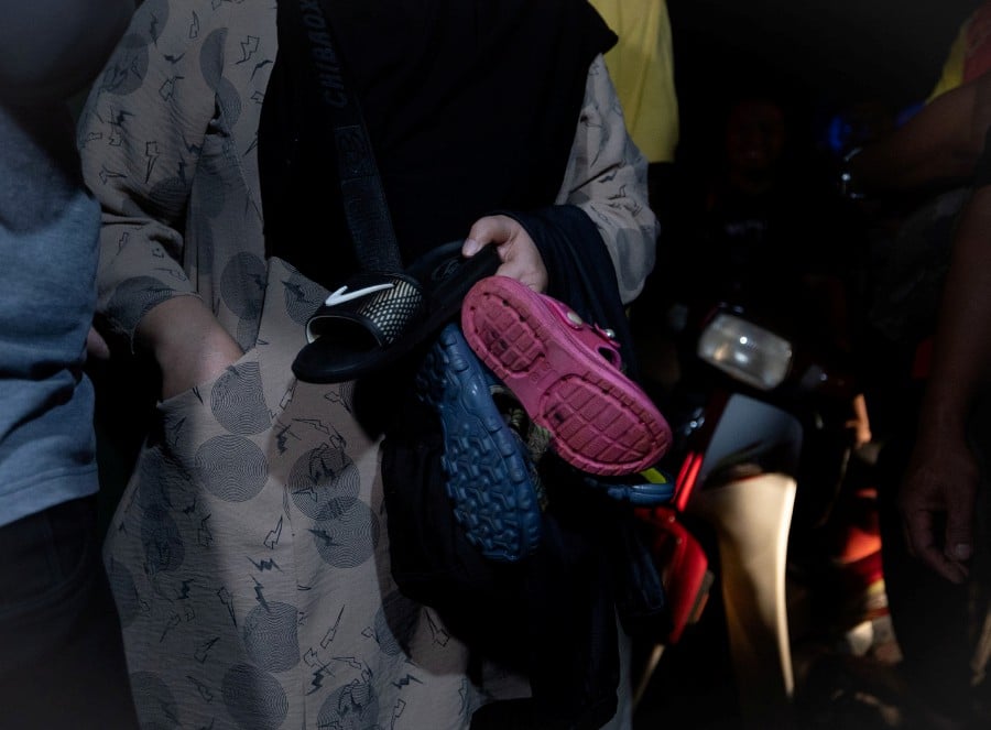  Ainur Raden Mustafa Amiruddin, 51, the aunt of one of the drowned victims, holding a pair of child’s shoes and trousers following the discovery of a boy’s body at 9.50 pm last night at Sungai Kenjur, Kampung Poh, Bidor.- Bernama pic