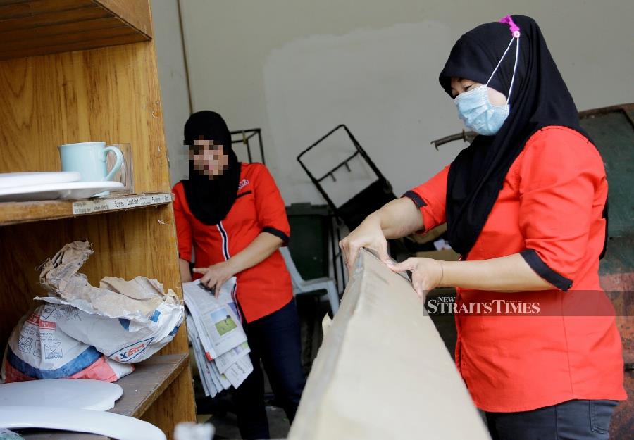  Two Indonesian women in headscarves and face masks negotiate a salary while standing in a storeroom.