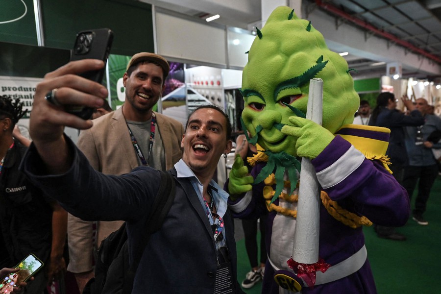 A visitor takes a selfie picture with a person in a costume of a cola of a cannabis plant during the Cannabis Expo Brazil, a hemp and cannabis industry exhibition, in Sao Paulo, Brazil. - AFP PIC