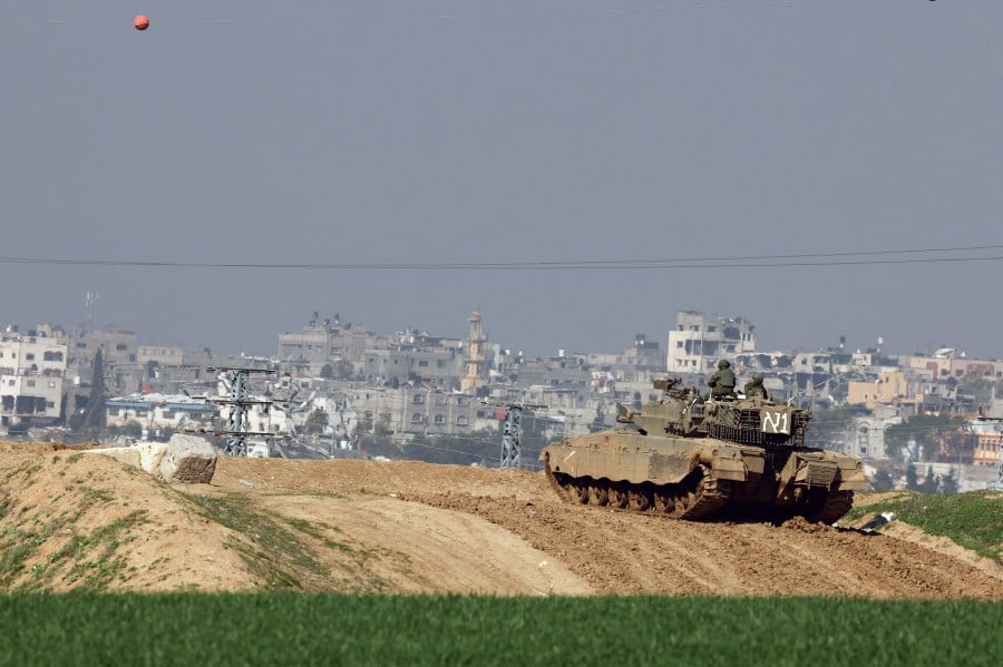 A picture taken from a position in southern Israel along the border with the Gaza Strip on January 19, 2024, shows an Israeli tank along the fence as damaged buildings are see in the Gaza Strip. - AFP PIC