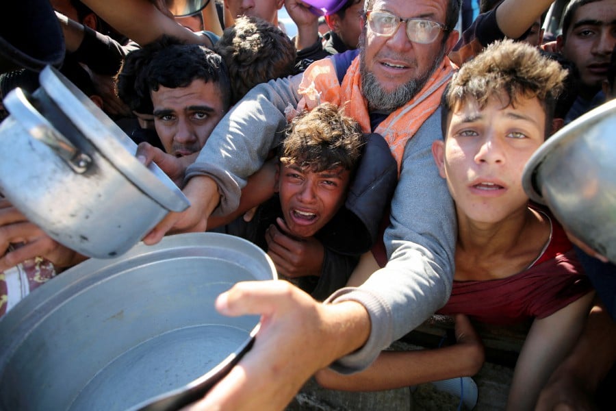 Palestinians gather to receive food cooked by a charity kitchen, amid a hunger crisis as the Israel-Gaza conflict continues, in Khan Younis in the southern Gaza Strip. -- REUTERS PIC