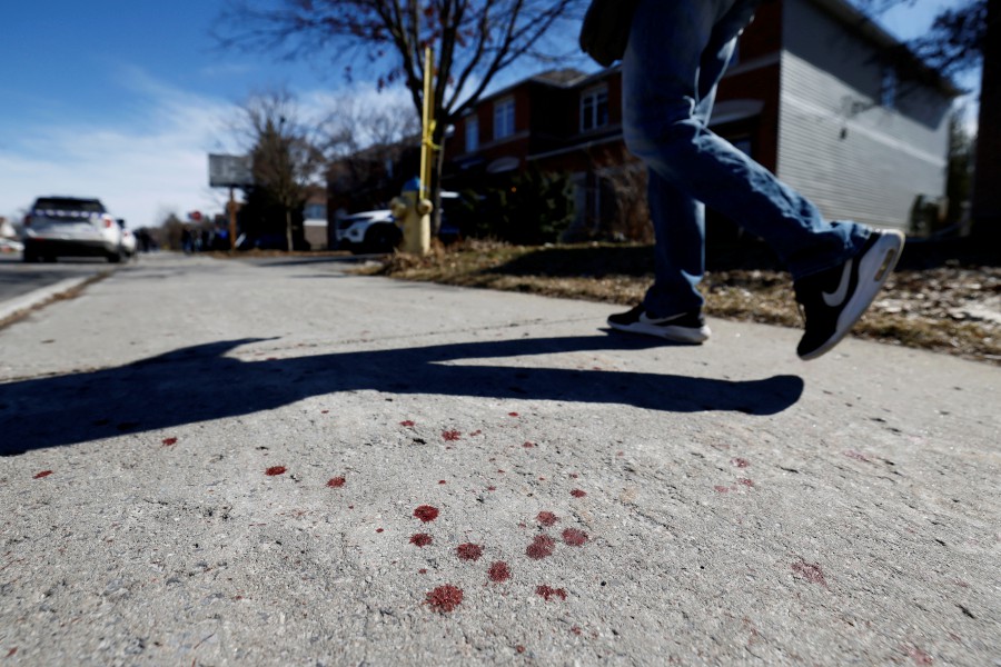 A pedestrian walks past blood splatter on a sidewalk after four children and two adults were found dead inside a nearby house in the Ottawa suburb of Barrhaven, Ontario, Canada. -- REUTERS