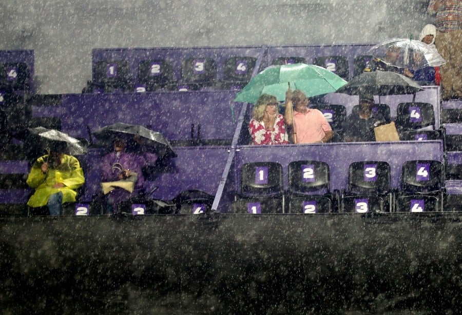 Fans in the stands take cover from bad weather as the semifinal match between Poland's Iga Swiatek and Belarus' Aryna Sabalenka is suspended due to rain. -REUTERS/Henry Romero