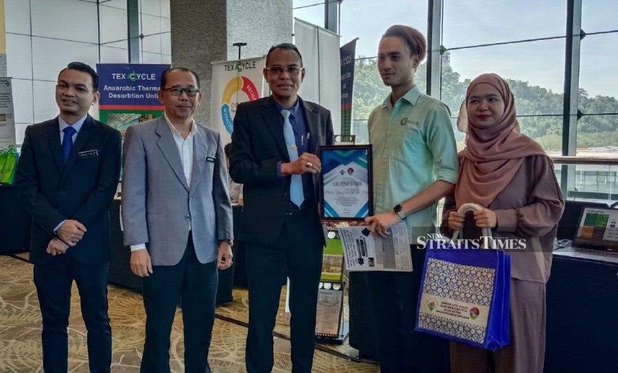 National Environment department director-general Datuk Wan Abdul Latiff Wan Jaafar (centre) presenting a certificate of participation to one of the exhibitors in conjunction with Environmental Quality Act 1974 seminar at Sabah International Convention Centre here. Present was Sabah Environment director Amirul Aripin (second left). -NSTP/OLIVIA MIWIL