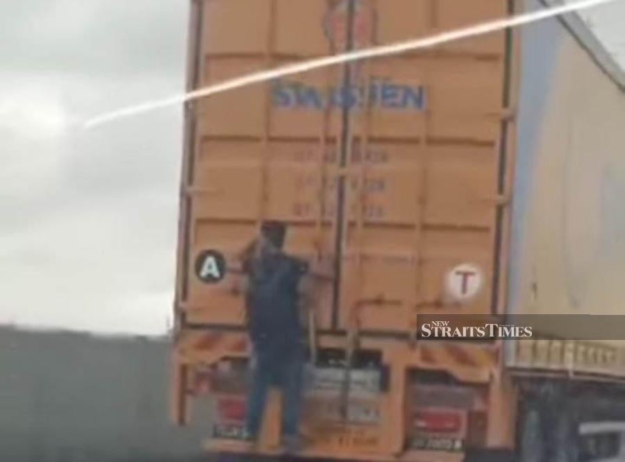 Screengrab of a viral video on social media showing a man clinging onto the rear of a moving trailer. -PIC CREDIT: HARIAN METRO