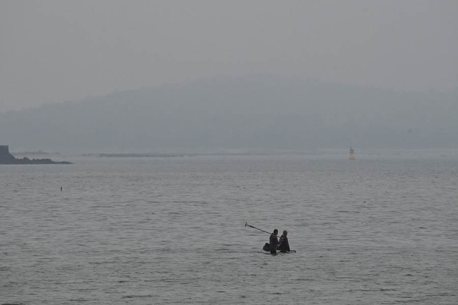 Fishermen wade in the sea off a beach in Xiamen with the Taiwanese island of Kinmen visible in the distance, in southeast China’s Fujian province on May 23, 2024. As Beijing's ships and warplanes encircled Taiwan on May 23, television anchors on the self-ruled island focused instead on a store razed by fire, a proposed ban on ambulance sirens, and a restaurant scandal involving an influencer. -AFP/Greg Baker